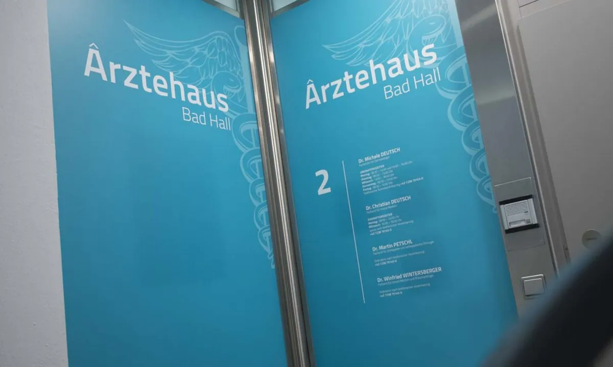 Eingangstür des Ärztehaus Bad Hall mit Logo und Tafel der Ordinationen im 2. Stock